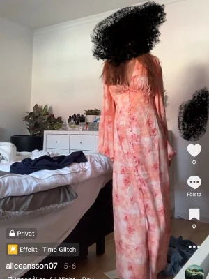 Lång blommig klänning med v-ringning - Säljer en lång klänning med blommigt mönster i rosa och orange toner. Klänningen har v-ringning, långa ärmar och knappar framtill. Perfekt för sommarens alla tillfällen och har en luftig, flowy passform. Skickar samma dag.🌺💞