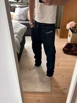 Mörkblå jeans från Diesel - Säljer ett par mörkblå jeans från Diesel med klassisk femficksmodell och kontrastsömmar. Jeansen har en rak passform och detaljerad etikett bak i midjan. Perfekta för dig som gillar en tidlös och avslappnad stil. Knappt använda, nypris ca 1500