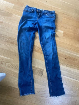 Blå skinny jeans från Denim United - Säljer ett par blå skinny jeans från Denim United med råa, avklippta benslut och klassisk femficksdesign. Jeansen har orange kontrastsömmar och är tillverkade i stretchig denim för en bekväm passform. Perfekta till vardags för en avslappnad look.