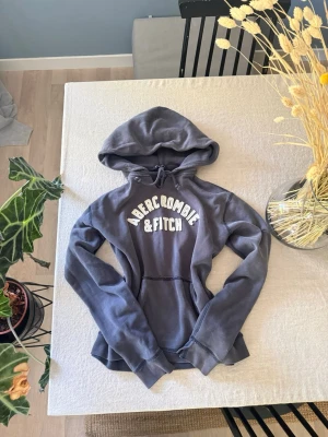 Blå hoodie från Abercrombie & Fitch - Mörkblå hoodie från Abercrombie & Fitch med stor vit logga på bröstet. 