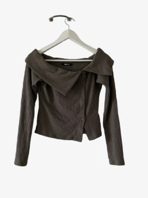 Brun ribbad offshoulder topp🌸 - Trendig brun ribbad topp från Urban Chic med offshoulder-design och stora krage. Toppen har långa ärmar och knappar framtill, perfekt för dig som vill sticka ut med en unik detalj. Snygg att styla med både jeans och kjol.