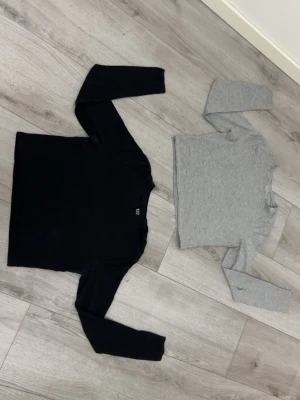 Två långärmade baströjor - Säljer två långärmade toppar i basic stil, en i svart och en i ljusgrått. Båda har rund halsringning och är tillverkade i mjukt, stretchigt material som passar perfekt till lager på lager eller som enkla vardagsplagg.