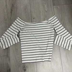 Randig offshoulder topp - Snygg vit offshoulder topp med svarta horisontella ränder och trekvartsärm. Perfekt till jeans eller kjol för en trendig look. Mjuk och stretchig känsla.