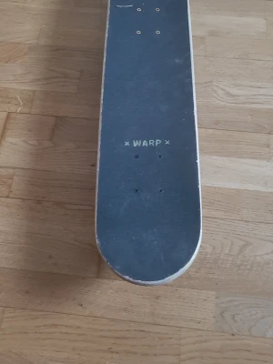 Svart skateboard från Warp - Skateboard från Warp med svart griptape och vit kant. Brädan har klassisk form och fyra hjul undertill. Perfekt för dig som vill cruisa eller öva tricks i parken.