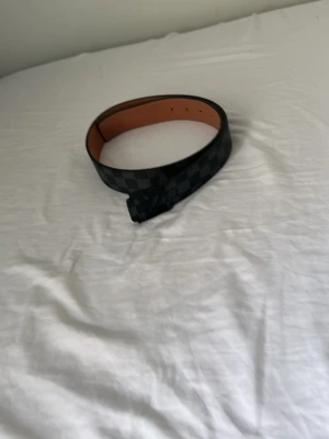 Svart rutigt bälte - Snyggt svart bälte med klassiskt rutigt mönster och svart spänne. Bältet har en insida i brunt skinn och passar perfekt till jeans eller byxor för en stilren look.