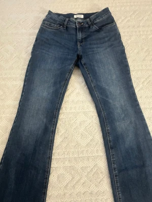Blå bootcut jeans med klassisk tvätt - Snygga blå bootcut jeans med klassisk tvätt och femficksmodell. Jeansen har normal midja och lätt slitna detaljer framtill och baktill. Perfekta för en avslappnad och trendig look. Materialet är denim i bomull med lite stretch för extra komfort.