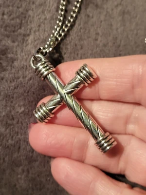Kedjehalsband med kors i silverfärg - Snyggt halsband i rostfritt stål med ett stort kors i silverfärgad metall. Korset har ett tvinnat mönster och detaljerade ringar vid ändarna, vilket ger en cool och robust look. Hängs på en grov kedja som matchar stilen perfekt. Perfekt accessoar för dig som gillar statement-smycken.