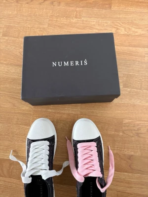Svarta Numeris sneakers med vita och rosa snören - Snygga svarta sneakers från Numeris med vita tåpartier och kontrasterande skosnören – ett vitt och ett rosa. ÖPPEN FÖR PRIS FÖRSLAG 