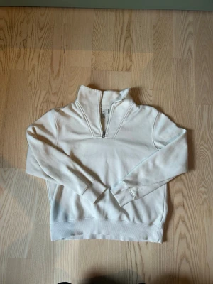 Vit halvzip hoodie från H&M - Snygg vit hoodie från H&M med halvzip och hög krage. Regular fit och tillverkad i mjukt bomullsmaterial. Perfekt för en avslappnad och stilren look. Långa ärmar och ribbade muddar ger en klassisk känsla.