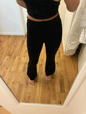 Svarta mjukisbyxor med utsvängda ben - Säljer ett par svarta mjukisbyxor med utsvängda ben och hög midja. Byxorna har en enkel och clean look, perfekta för chill dagar hemma eller när du vill vara bekväm. Mjukt och stretchigt material som sitter skönt på kroppen.