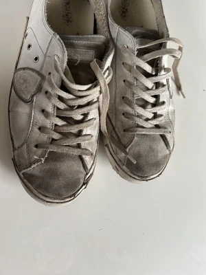 Philippe Model vita sneakers - Snygga vita sneakers från Philippe Model med klassisk låg siluett. Skorna har vita skosnören, detaljer i mocka samt en brun sula. Säljer dem billigt p.gr av att jag vill ha bort dem!