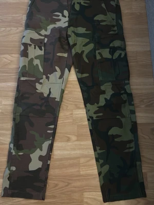 Camo cargobyxor från Levi's - Säljer ett par cargobyxor från Levi's i klassiskt camomönster med gröna, bruna och beige toner. Byxorna har flera stora fickor på sidorna och en relaxed passform. Perfekta för en streetwear-look och riktigt sköna till vardags.