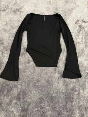 Svart långärmad topp med utsvängda ärmar - Trendig svart långärmad topp med utsvängda ärmar och fyrkantig ringning. Figurnära passform och mjukt stretchigt material, perfekt att styla till jeans eller kjol. Enkel men snygg design som ger en cool vibe.