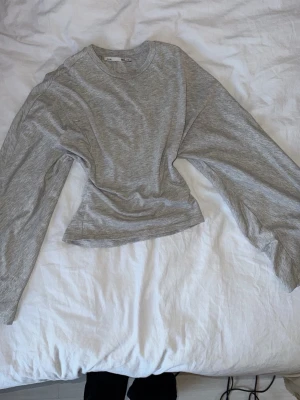 Grå långärmad topp från H&M - En enkel och stilren grå långärmad topp från H&M. Tillverkad i mjukt och stretchigt bomullsmaterial med rund halsringning och avslappnad passform. Perfekt basplagg att matcha med allt.