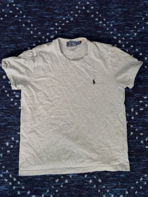 Grå t-shirt från Polo Ralph Lauren - Klassisk grå t-shirt från Polo Ralph Lauren med liten broderad logga på bröstet. T-shirten har rund halsringning och korta ärmar. Perfekt basic-plagg som funkar till allt och är gjord i mjuk bomull.
