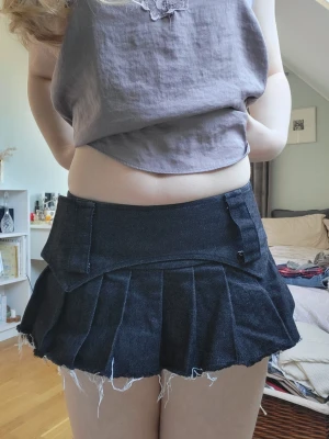 Svart plisserad jeanskjol, med minsshorts under - Köpt från asteraceae.vn , inga defekter, strlk S, men skulle absolut säga xs.🥰Cool svart kort jeanskjol med plisserad design och rå, fransig nederkant. Kjolen har bred linning och bälteshällor, perfekt för en edgy look. Passar dig som gillar streetstyle och vill ha något unikt i garderoben.