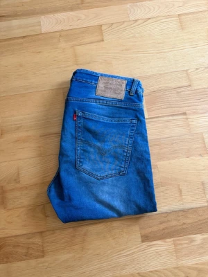 Levi's 523 blå jeans herr - Säljer ett par klassiska blå Levi's 523 jeans i 100% bomull. De har en slim/rak passform, fem fickor och den ikoniska läderlappen bak i midjan. Perfekta för dig som gillar tidlös denimstil och vill ha ett par jeans som alltid funkar.