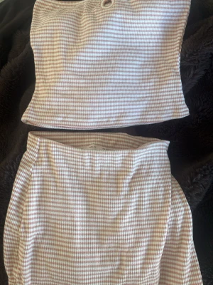Rosa och vitrandigt set från Nelly - Sött tvådelat set från Newbie i mjukt ribbat material. Setet består av ett linne och ett par shorts i rosa och vitrandigt mönster. Linnet har en liten rosett och dekorativ ring framtill. Perfekt för en mysig dag hemma. Toppen i M men är väldigt liten.