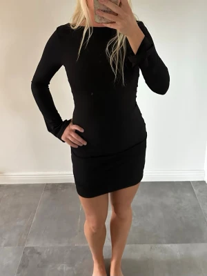 Bikbok Svart långärmad miniklänning med öppen rygg - Snygg svart miniklänning med lång ärm och öppen rygg från BikBok. Klänningen har en tight passform och enkel, stilren design som framhäver figuren. Storlek S. Helt oanvänd med prislapp kvar. Nypris 499kr- säljer för 200kr.