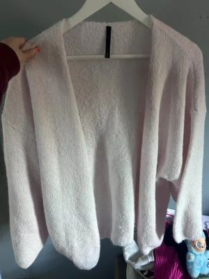 Ljusrosa öppen kofta - Mysig ljusrosa kofta med öppen front och avslappnad passform. Koftan är stickad i ett mjukt material och har långa ärmar. Perfekt att slänga på sig för en chill look.
