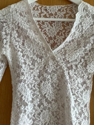Vit spetsblus med v-ringning - Superfin vit blus i spets med v-ringning och lång ärm. Blusen har ett blommigt spetsmönster och är lätt transparent. 
