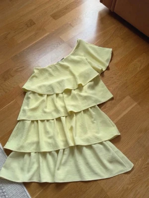  Populär Gul offshoulder volangklänning - Säljer en ljusgul klänning med flera volanglager och offshoulder-design. Klänningen har en asymmetrisk axel och är tillverkad i ett lätt tyg som passar perfekt för varma dagar. Supersöt och trendig modell med flowy känsla.