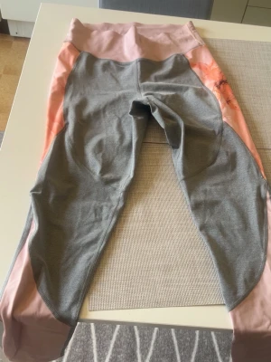 Grå och rosa leggings med hög midja - Snygga leggings i grått och ljusrosa med hög midja och kontrastpaneler längs sidorna. Stretchigt material som sitter skönt och följer kroppen. Perfekta för träning eller chill. Inga synliga loggor eller märken.