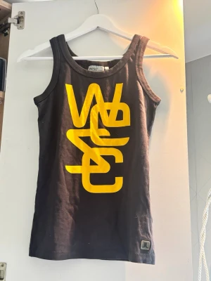 Svart linnetopp från WESC med tryck - Snygg svart linnetopp från WESC med stort gult grafiskt tryck framtill. Klassisk rund halsringning och ärmlös design. Storleken säger XXS men skulle snarare säga XS/S. 