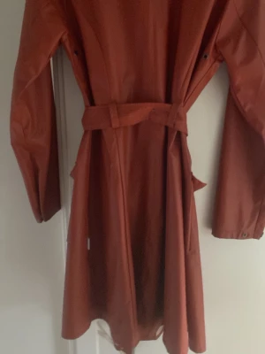 Rostbrun regnjacka med bälte - Snygg rostbrun regnjacka i längre modell som trenchcoat