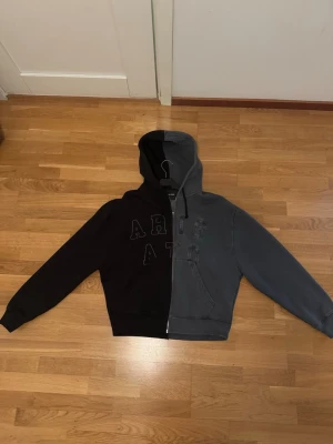 Tvåfärgad hoodie från Axel Arigato - Unik hoodie från Axel Arigato i två färger, svart och grå, med dragkedja framtill och huva. Tillverkad i 100% ekologisk bomull. Säljer på grund av att jag inte använder den mer.