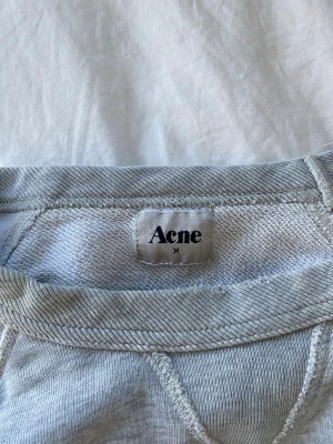 Ljusgrå sweatshirt från Acne - Ljusgrå sweatshirt från Acne med klassisk rund halsringning och ribbade muddar vid ärmslut och nederkant. Tröjan har en avslappnad passform och är tillverkad i mjukt bomullsmaterial. Perfekt för en chill och stilren look.