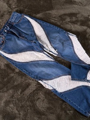Blå Weekday jeans med fransdetaljer - Unika blå jeans från Weekday med vågformade fransdetaljer i vitt längs benen. Modellen heter Thursday Jeans och har en cool, trendig look med kontrasterande denim och fransar. Perfekta för dig som vill sticka ut och gillar statement-plagg.