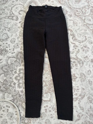 Svarta ribbade leggings med hög midja - Snygga svarta leggings med hög midja och ribbad struktur. De har en tight passform och är perfekta för en trendig och bekväm look. Materialet är stretchigt och följsamt, vilket gör dem sköna att bära hela dagen.