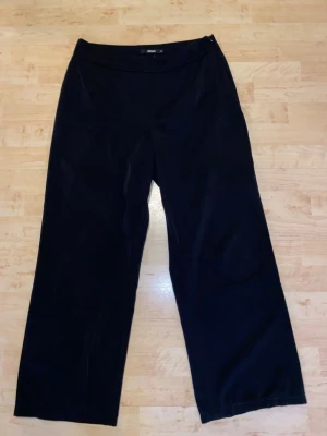 Svarta kostymbyxor från Bik Bok - Stilrena svarta kostymbyxor från Bik Bok med rak passform och hög midja. Byxorna har en enkel design utan synliga fickor eller detaljer, vilket ger en clean och modern look. Perfekta till en dressad outfit. Materialet känns mjukt och följsamt.