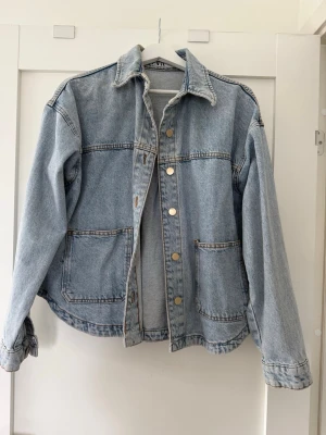 Ljusblå  jeansjacka Zara  - Säljer en oversized ljusblå jeansjacka med klassisk krage, stora framfickor och silverfärgade knappar. Jackan har en avslappnad passform och nedhasade axlar för en cool och trendig look. Perfekt att slänga över en hoodie eller t-shirt.