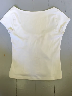 Vit tight topp med öppet bak på ryggen - En enkel och stilren vit topp med tight passform och öppet på ryggen. Kortärmad modell i mjukt material som passar perfekt till jeans eller kjol. Snygg basic som funkar till många olika looks.