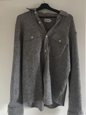 Grå overshirt från East West - Snygg grå overshirt från East West med två bröstfickor och vita knappar. Overshirten  har lång ärm och är tillverkad i ett mjukt material som passar perfekt till lager på lager-stil.