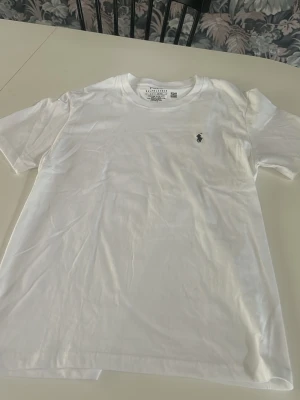 Vit t-shirt från Polo Ralph Lauren - Klassisk vit t-shirt från Polo Ralph Lauren med rund halsringning och den ikoniska broderade loggan på bröstet. Tillverkad i mjuk bomull och har en normal passform. Perfekt basplagg för alla tillfällen.