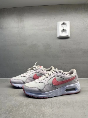 Nike Air Max vita och rosa sneakers - Säljer ett par Nike Air Max SC i storlek 39, i väldigt fint skick! Snygga rosa och vita sneakers med den klassiska Air Max-designen – både bekväma och trendiga.  Skorna är i väldigt fint skick, fräscha och välvårdade, med luftig mesh och slitstarka detaljer. De har en dämpande Air Max-sula som ger extra komfort och passar perfekt för vardag, promenader eller gym.