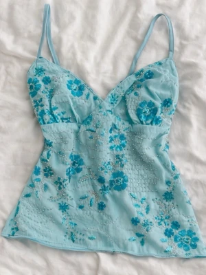 Y2K Ibiza-inspirerad ljusblå topp med broderi & pärlor - Superfin Y2K-topp i ljusblå färg med blomsterbroderier och pärldetaljer ✨ Figurnära passform med tunna spaghettiband – väldigt smickrande på.  Ger starka Ibiza / beach club / sommarkväll-vibes 🌊💙 Perfekt till semester, solnedgångsmiddagar, strandfester eller festivaler. Lätt att styla med linnebyxor, lågmidjade jeans eller en luftig kjol.  • Skick: mycket fint / ny utan prislapp • Storlek: XS–S (S / 36 / 8) • Färg: ljusblå • Stil: Y2K / Ibiza / Coquette / Fairy  Snabb frakt ❤️ 