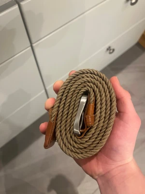 Beige flätat bälte från Jack & Jones 105 - Snyggt beige flätat bälte från Jack & Jones med detaljer i brunt skinn och ett silvrigt metallspänne. Perfekt accessoar för att lyfta din outfit och funkar till både jeans och chinos. 105 cm. Som man kan se på andra bilden har en tygglapp gått av, dock påverkar det inget, annars har den inga andra defekter.