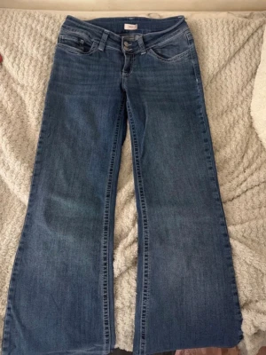 Blå bootcut jeans med broderade fickor - Säljer ett par lågmidjade blå bootcut jeans från Nelly med snygga broderade detaljer på bakfickorna. Jeansen har lågmidjad passform och är tillverkade i bomull, perfekta för en avslappnad och trendig look.