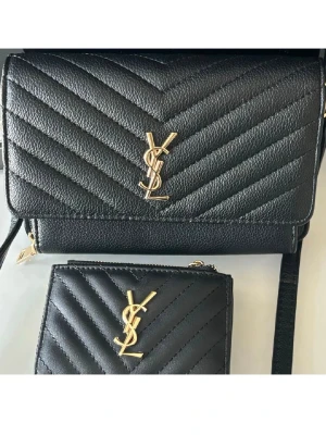 Svart handväska i läder - Snygg svart handväska med guldfärgade detaljer. Väskan har axelrem och dragkedja samt elegant kedjedetalj. Perfekt för dig som vill ha en stilren och lyxig accessoar. Nyskick!