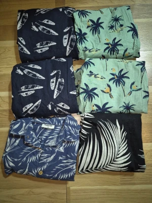  Barn Mönstrade skjortor med tropiskt tema stl 134 - Säljer flera skjortor  6st med tropiska och naturinspirerade mönster i blått, grönt och svart. Skjortorna har krage och knappar framtill, vissa med palmblad och papegojor, andra med surfbrädor. Perfekta för dig som gillar färg och mönster!
