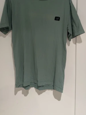 Grön t-shirt från C.P. Company - Snygg grön t-shirt från C.P. Company med diskret logga på bröstet. Klassisk passform och rund halsringning. Perfekt basplagg till garderoben och enkel att matcha med olika stilar.
