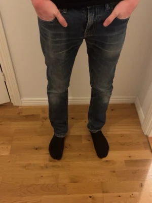 Blå Levi's jeans med raka ben - Säljer ett par klassiska blå jeans från Levi's med raka ben och snygga slitningar. Jeansen har fem fickor, normal midja och en diskret tvättad look. Perfekta för en avslappnad stil och passar till det mesta. Skriv för mer info