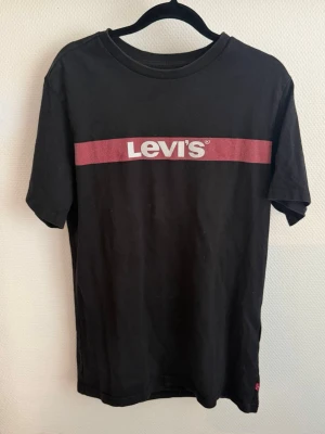 Levi's t-shirt - Snygg svart t-shirt från Levi's med klassisk röd logga och vit text över bröstet. T-shirten har rund halsringning och korta ärmar. Tillverkad i mjuk bomull för en bekväm känsla. Använd endast ett fåtal gånger. 