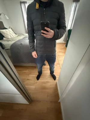Parajumpers Jacka - Snygg mörkgrå pufferjacka med quiltad design och hög krage. Jackan har en gul detalj vid dragkedjan och två sidofickor. Perfekt för kalla dagar och ger en clean look. Passar dig som gillar stilrena ytterplagg.