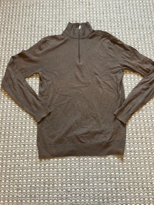 Brun tunnstickad tröja med halv dragkedja - Snygg brun tunnstickad tröja med halv dragkedja och hög krage. Tröjan har långa ärmar och ribbade muddar vid ärmslut och nederkant. Perfekt för lager på lager och enkel att matcha med olika outfits. Den är i snytt skick och har använt bara några få gånger!! Pris kan diskuteras