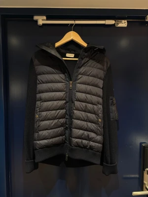 Marinblå Moncler Cardigan - Marinblå cardigan från Moncler. Jackan har dragkedja framtill, fickor med tryckknappar och en ficka på ärmen. Små tendenser till tovning på ullen längst ner baktill. Samt precis vid dragkedjan. Annars är jackan i fint skick och har blivit väl omhändertagen under tiden jag ägt den. Kommer till Monclers hemsida via QR kod i jackan. 